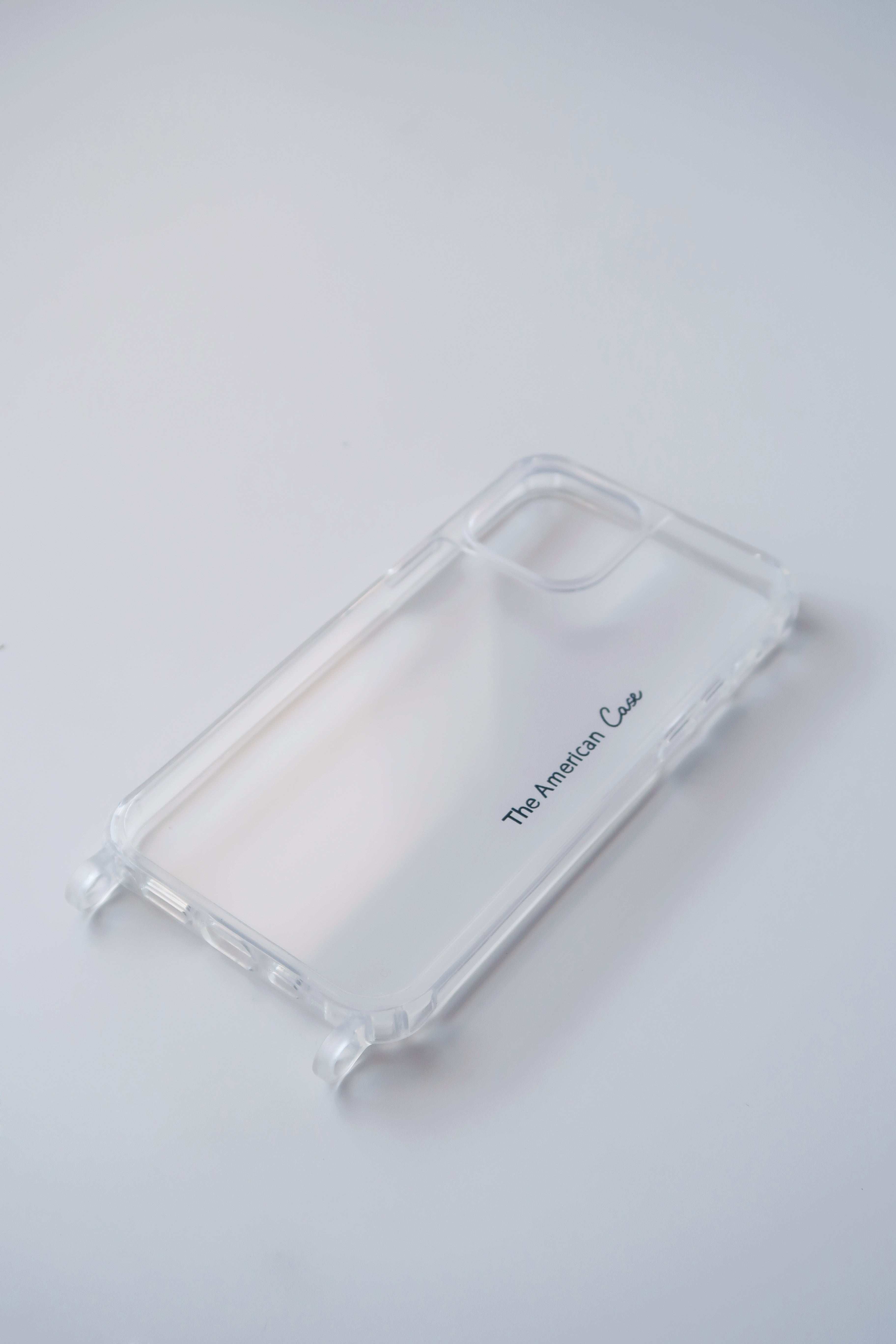 an angle view of a clear silicon phone case with two silicon rings with The American Case logo. The case features precise cutouts for buttons, speakers, and camera lenses, allowing full access to the phone's features. It can be easily attached to phone chains with carabiners for added convenience.
