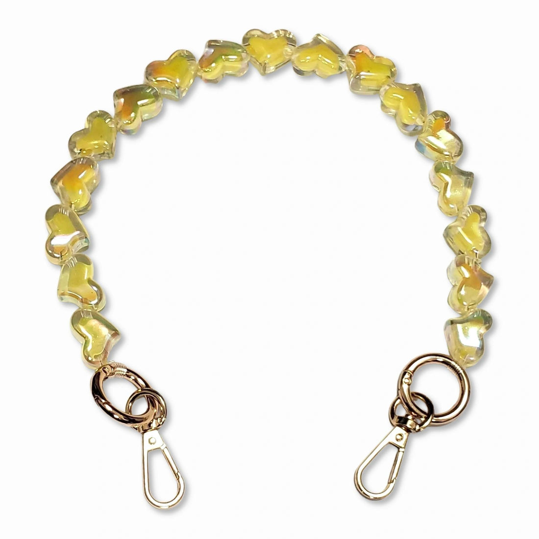 A short bead chain with golden carabiners and a glittery heart charm in yellow color. The chain is designed to be attached to a phone case and can be worn around the wrist for a playful and eye-catching look. The chain is made by The American Case and is designed to be durable.