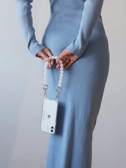 a Pastel white Crackle Bead Short Phone Chain with Golden Carabiners attache to a clear phone case with The American Case print hold by a lady by her hand