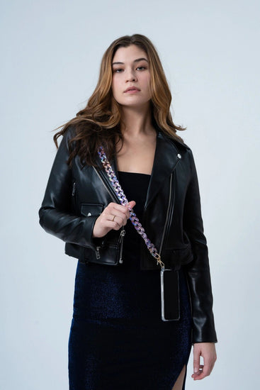 A woman wearing a crystal-effect resin phone chain with gold buckle details, which can be worn across body for added convenience. The chain adds a glamorous touch to her dark jacket.