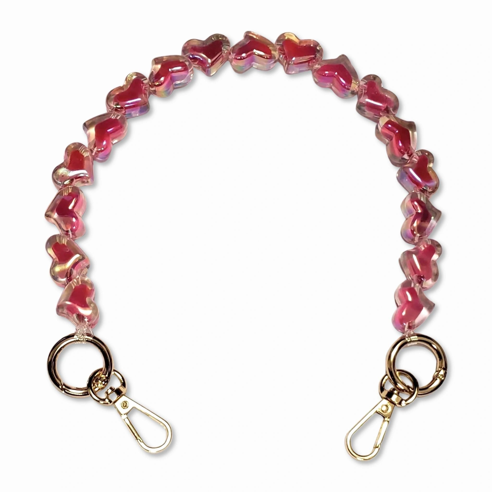 A short bead chain with golden carabiners and a glittery heart charm in deep pink color. The chain is designed to be attached to a phone case and can be worn around the wrist for a playful and eye-catching look. The chain is made by The American Case and is designed to be durable.